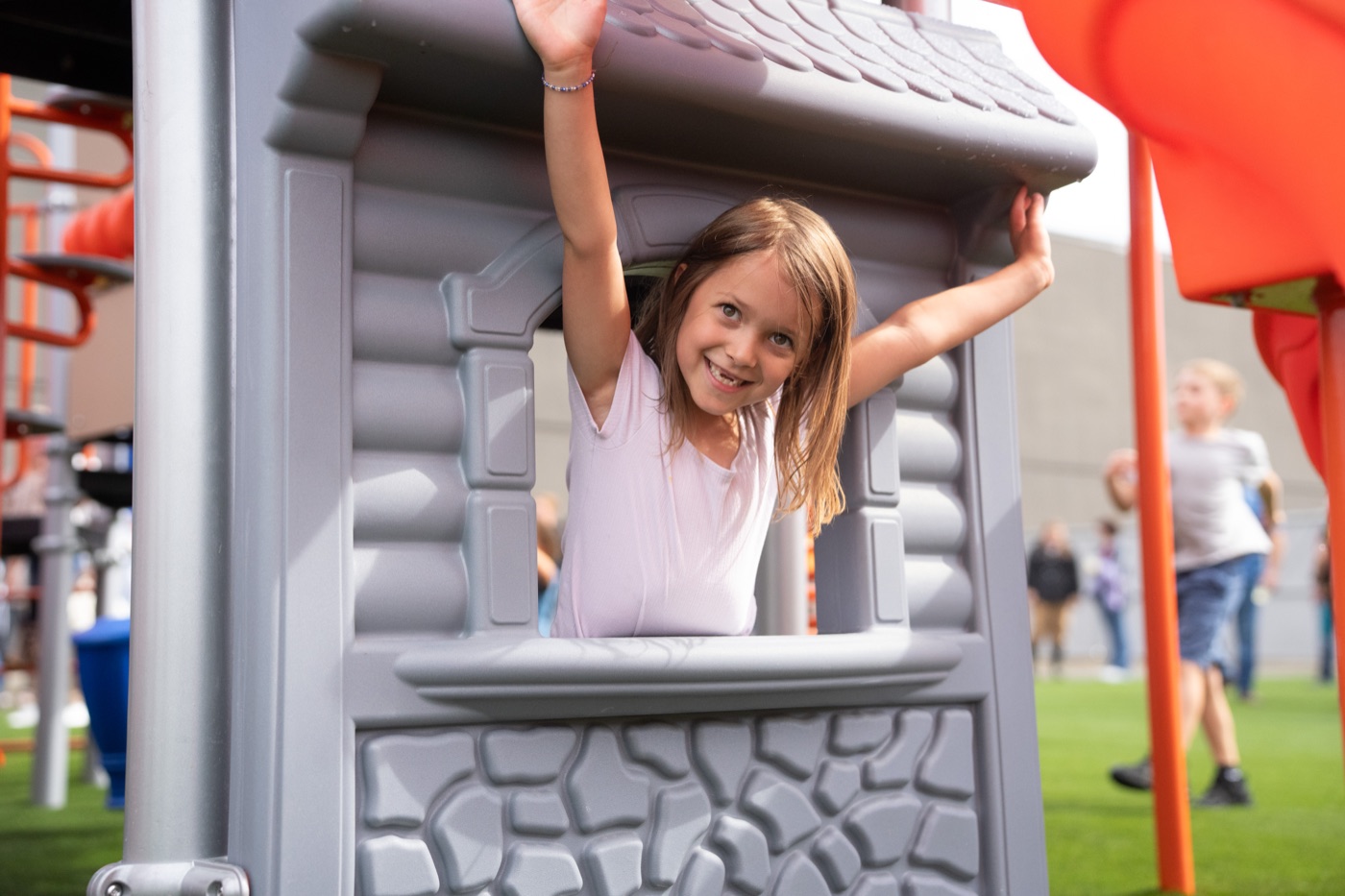 A smiling girl peeking through the playhouse window on the Sun City CDC playground
